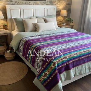 May include: A bed with a white headboard is covered with a purple, teal, and white patterned blanket. The blanket has the words "ANDEAN ALPACA" printed on it. The bed is made up with several pillows and a light green bedspread.