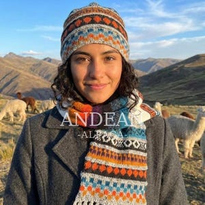 Puede incluir: Un gorro de punto y una bufanda a juego con un patrón geométrico multicolor en tonos naranja, azul, gris y negro. La bufanda muestra el texto ANDEAN ALPACA en letras blancas en el centro del diseño de la tela tejida.