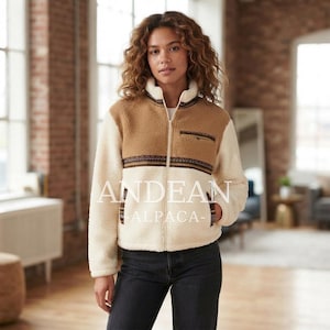 May include: A zip-up fleece jacket featuring a colour-blocked design with a tan upper section and cream lower section. A horizontal patterned band with geometric details separates the colours. The text ANDEAN ALPACA is visible.