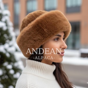 Könnte beinhalten: Ein brauner Kunstpelzhut mit breiter Krempe, mit dem Text "ANDEAN -ALPACA-". Der Hut wird mit einem weißen Rollkragenpullover getragen. Der Hut wirkt weich und warm, geeignet für kaltes Wetter.