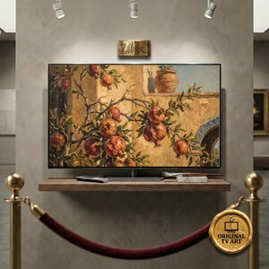 Peut inclure: Une grande télévision à écran plat affichant une peinture de grenades sur une branche. L'œuvre d'art présente une palette de couleurs chaudes avec des oranges, des bruns et des verts. La télévision est montée sur une étagère en bois.