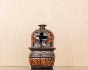 May include: A brown ceramic incense burner with orange floral designs. The burner has a cross-shaped opening on the top and a round base.
