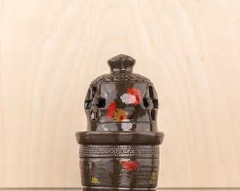 May include: A brown ceramic incense burner with a floral design. The burner has a round base and a domed top with cutouts. The floral design features red, yellow, and green flowers.