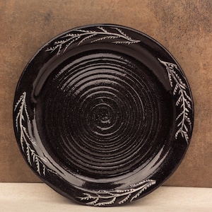 Peut inclure: Une assiette en céramique noire avec un motif en spirale blanc et un motif floral blanc autour du bord.