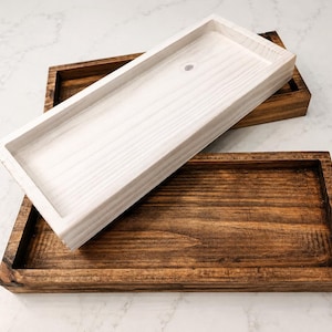 May include: Two rectangular wooden trays with raised edges. One tray features a dark brown stained finish with visible wood grain, while the other is positioned on top and has a light white-washed finish with a small circular hole in the base.