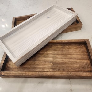 May include: Two wooden trays, one white and one brown, are stacked on top of each other. The white tray is on top and the brown tray is on the bottom.