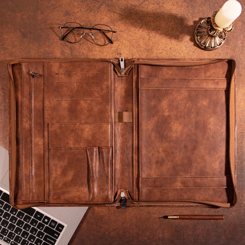 May include: A brown leather portfolio with multiple pockets and a zipper closure. The portfolio is open and lying flat on a brown surface.