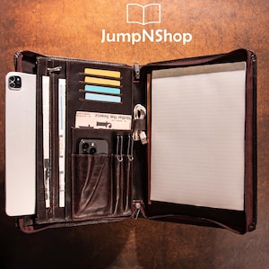 May include: Open brown leather portfolio with multiple compartments, including card slots, a phone pocket, and a notepad. The portfolio contains a tablet, cards, a phone, and a notepad. The JumpNShop logo is visible in the top center.