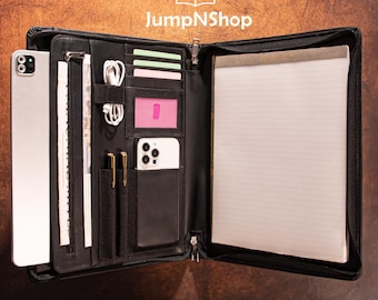 May include: Black leather portfolio with multiple compartments, including slots for cards, a phone, and pens. A notepad and a tablet are also visible. The JumpNShop logo is at the top.