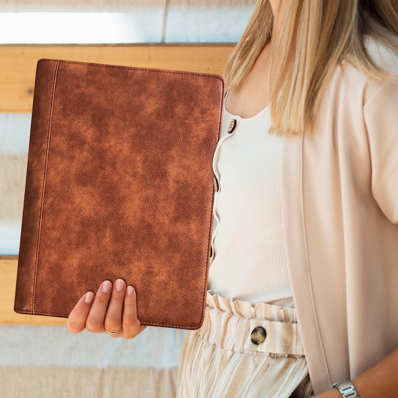 May include: A brown leather binder with a textured surface. The binder is closed and has a gold metal clasp.