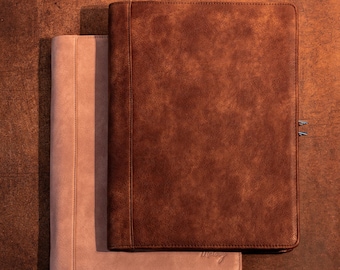 May include: Two leather portfolios in shades of brown and tan. The larger portfolio is a rich, textured brown with a metal clasp. The smaller portfolio is a light tan color. Both are rectangular and appear to be closed.