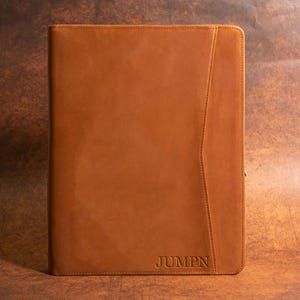 May include: A brown leather portfolio with a stitched design and the word "JUMPN" embossed on the front.