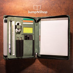 May include: A green leather zippered portfolio with multiple pockets and compartments. The portfolio is open to reveal a notepad with a grid pattern, a phone case, and a pen holder.