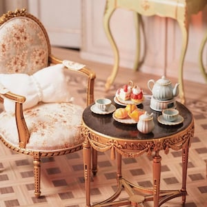 May include: Miniature tea set on a small, ornate table with a black top and gold trim. The table is set with a teapot, teacups, and a plate of pastries. A matching chair with floral upholstery and gold accents is nearby.