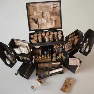 Op de afbeelding: Een zwarte, multi-compartiment box, die doet denken aan een vintage apothekerskit, is open om de inhoud te onthullen. Het bevat tal van kleine glazen flesjes met kurken, flesjes en opgerold papier. De doos is gevuld met diverse items.