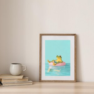 May include: A framed illustration of a green frog wearing blue shorts and relaxing on a pink inflatable ring in a blue pool with a reflection of the ring in the water.