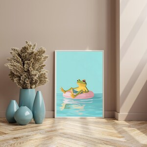 May include: A green frog wearing a blue swimsuit floats on a pink inflatable ring in a blue pool. The frog is looking to the right and has its legs crossed. The background is a light blue.