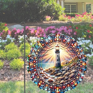 May include: A round garden flag featuring a lighthouse scene. The lighthouse is depicted with a bright light emanating from the top, surrounded by a colorful, mosaic-like border. The flag is displayed on a black metal stand, set against a backdrop of flowers and greenery.