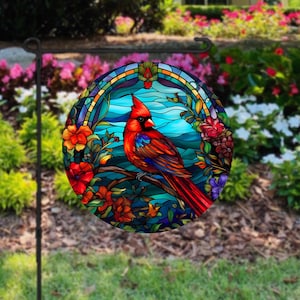 May include: A stained glass style garden flag featuring a red cardinal bird perched on a branch with blue and green foliage and flowers. The flag is round and has a white background.