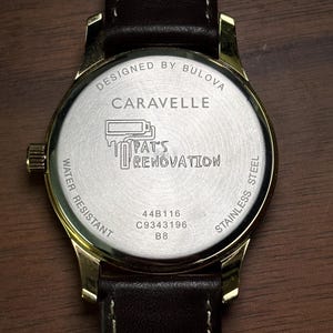 May include: Close-up of a gold-toned Caravelle watch with a brown leather strap. The watch face features the text "DESIGNED BY BULOVA", "CARAVELLE", and "PAT'S RENOVATION". The watch is water resistant and made of stainless steel.