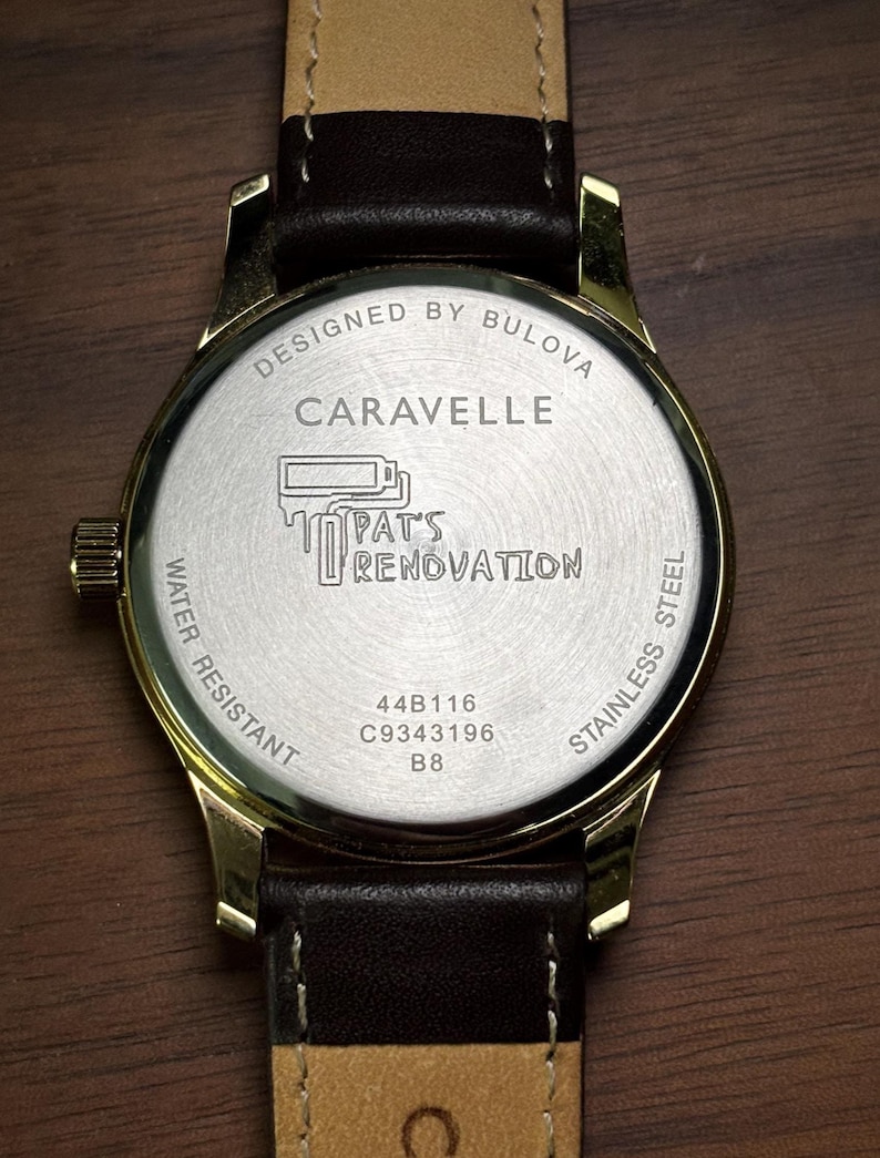 May include: Close-up of a gold-toned Caravelle watch with a brown leather strap. The watch face features the text "DESIGNED BY BULOVA", "CARAVELLE", and "PAT'S RENOVATION". The watch is water resistant and made of stainless steel.