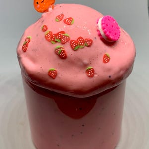May include: Pink slime with strawberry sprinkles and a pink and white cookie on top in a clear glass jar.