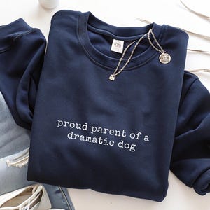 May include: A navy blue sweatshirt with the text "proud parent of a dramatic dog" in white.