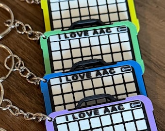 May include: A collection of seven rectangular keychains featuring a grid pattern and the text I LOVE AAC. Each keychain has a colored border in red, orange, yellow, green, blue, purple, or pink, and includes a silver metal split ring attached.