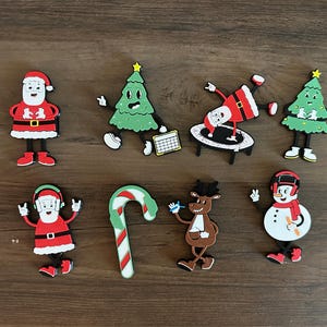 May include: A set of nine Christmas-themed ornaments featuring Santa Claus, a snowman, a reindeer, a candy cane, and Christmas trees. The ornaments are made of a colorful, rubber-like material.
