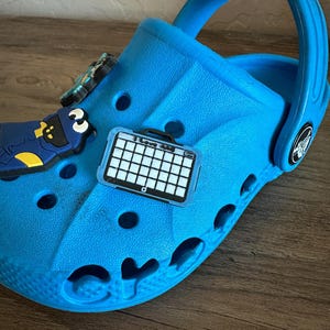 May include: Blue Crocs shoe with a black and white gridded charm and a blue Cookie Monster charm.