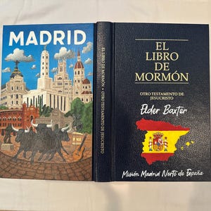 May include: A hardback book titled "EL LIBRO DE MORMON" in gold. The cover shows a painting of Madrid, Spain, and the back cover has a map of Spain with the Spanish flag.
