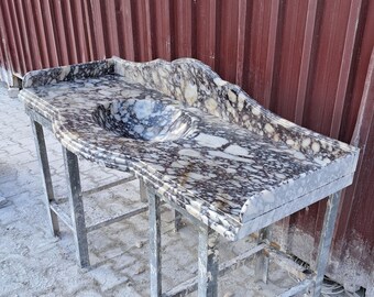 Può includere: Un piano da bagno in marmo bianco con un motivo a marmo bianco e nero. Il piano da bagno ha un bordo curvo e un lavabo integrato.