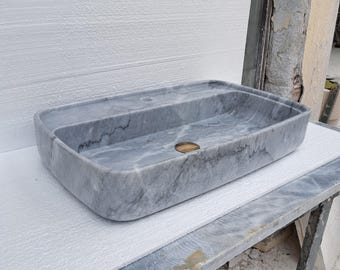 Puede incluir: Un lavabo de baño rectangular de mármol gris con un agujero de drenaje y un sutil patrón de vetas grises.