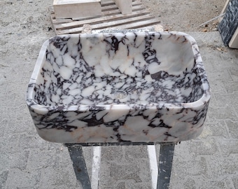 Può includere: Un lavandino in marmo bianco con venature viola e grigie. Il lavandino è su un supporto in metallo.