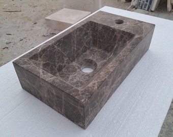 May include: A rectangular brown marble vessel sink with a single drain hole. The sink is set on a white surface.