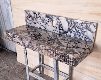 May include: A marble vanity unit with integrated sink and backsplash. The stone has a pattern of white and dark purple veining. The front edge of the vanity has a textured, ridged design. It is supported by a metal stand.