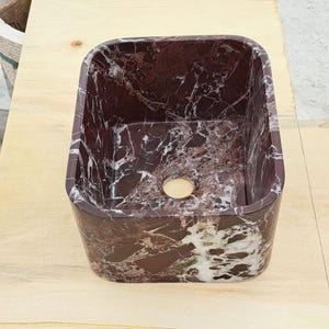 May include: A rectangular, burgundy marble sink with white veining. The sink has rounded corners and a circular drain hole. The sink is made of natural stone and is suitable for a bathroom or powder room.