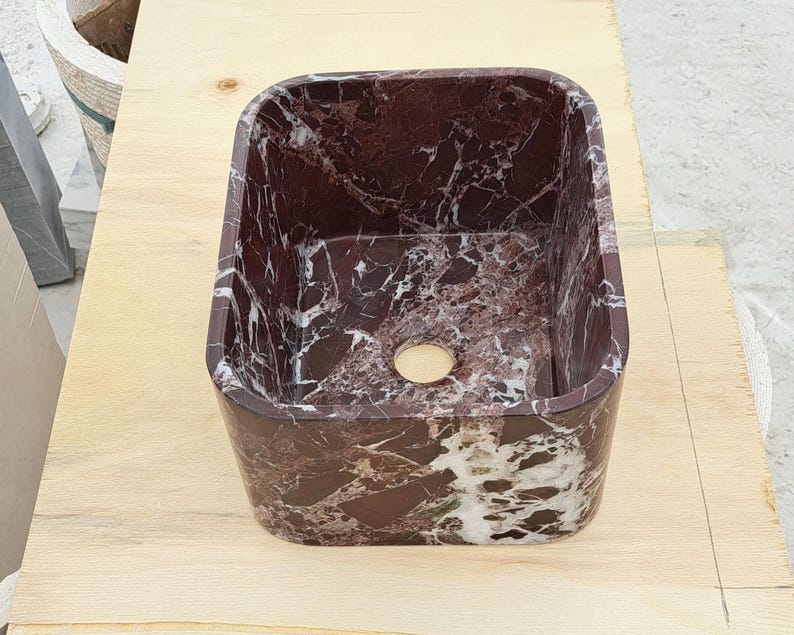 May include: A rectangular, burgundy marble sink with white veining. The sink has rounded corners and a circular drain hole. The sink is made of natural stone and is suitable for a bathroom or powder room.