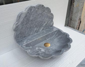 Puede incluir: Un lavabo de pared de mármol gris con un diseño de borde festoneado. El lavabo tiene un estante incorporado y un desagüe redondo de color dorado. El mármol tiene un veteado natural. El lavabo está diseñado para un baño. Medidas en centímetros.