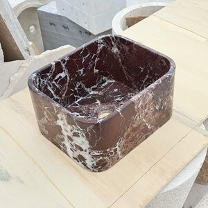 May include: A rectangular, dark red marble sink with white veining. The sink has a smooth, polished finish and a drain hole. The sink is a modern design and is suitable for a bathroom or powder room.