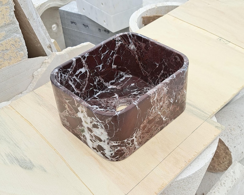 May include: A rectangular, dark red marble sink with white veining. The sink has a smooth, polished finish and a drain hole. The sink is a modern design and is suitable for a bathroom or powder room.