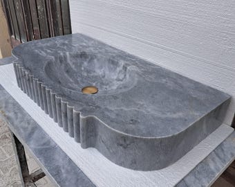 May include: A gray marble sink with a scalloped edge and a round basin. The sink is mounted on a white countertop.