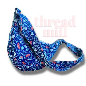 May include: A blue floral sling bag with a strap. The bag features a pattern of white, red, and light blue flowers and leaves on a dark blue background. The text "thread mill" is visible in the background.