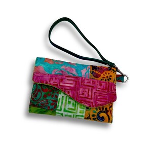 May include: A quilted wristlet pouch featuring a vibrant patchwork design with various geometric and floral patterns in shades of pink, orange, green, and blue. The bag includes a dark green wrist strap attached with a silver metal clasp.