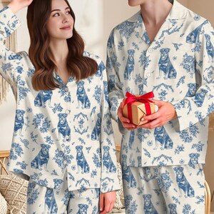 K&ouml;nnte beinhalten: Passende Schlafanz&uuml;ge in Creme mit blauem Hunde- und Blumenmuster. Die Sets bestehen aus einem Oberteil mit Kn&ouml;pfen und einer Hose. Die Schlafanz&uuml;ge werden von zwei Personen in einer gem&uuml;tlichen Innenumgebung getragen.