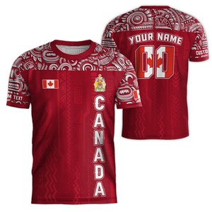 May include: Red and white t-shirt with a Polynesian-inspired design. The shirt features the Canadian flag, the Canadian coat of arms, and the word "CANADA" vertically down the right side. The back of the shirt has a white number "00" and the text "YOUR NAME".