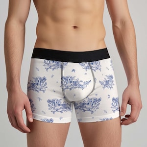 May include: Boxer briefs featuring a white base with a repeating blue toile-style pattern of dogs resting among foliage and small flowers. The garment includes a solid black elastic waistband and a contoured front pouch with visible stitching.