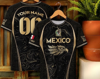 May include: Two black short-sleeve shirts with gold accents. The front shirt features the text MEXICO, a stylized eagle graphic, and a small Mexican flag. The back shirt displays the text YOUR NAME and the number 00 in large gold font.