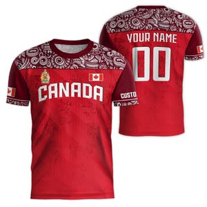 May include: Red and white short-sleeved jersey with a Canadian flag and the word "CANADA" printed on the front. The jersey has a white and red patterned design on the sleeves and collar. The back of the jersey has a white number "00" and the text "YOUR NAME" printed on it.