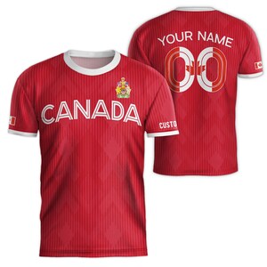 May include: Red and white soccer jersey with the word "CANADA" and a Canadian coat of arms on the front. The back of the jersey has a white number "00" with a Canadian flag on each side and the text "YOUR NAME" above the number.